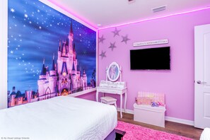 A bedroom with a Disney castle mural, a vanity with a mirror, a pink rug, and a sign on the wall.