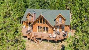A wooden cabin with a deck, surrounded by dense forest.