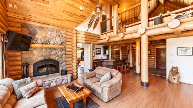 A log cabin interior with a stone fireplace, wooden furniture, and a balcony.