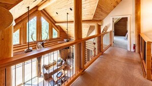 A wooden interior with a high ceiling, a balcony with a railing, and a view of the outdoors.