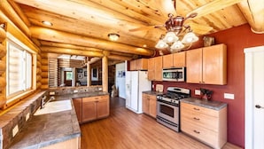 A log cabin kitchen with wooden cabinets, a stone countertop, a stove, and a ceiling fan.