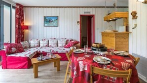 A cozy room with a red and white sofa set, a dining table set for four, and a wooden dresser with a mirror. - Baikonour by Interhome (Le Corbier)