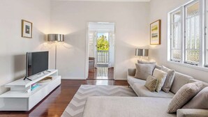 A modern living room with a flat-screen TV, a sofa, a coffee table, and two floor lamps. - Modern Twist + Old World Charm ~ 3Bed/2Bath/2Car (Kedron)
