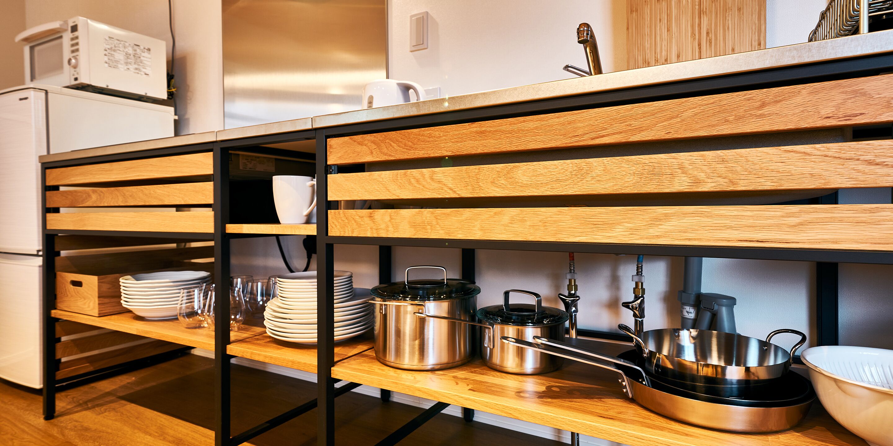 A kitchen with wooden shelves, a microwave, and various kitchen utensils.