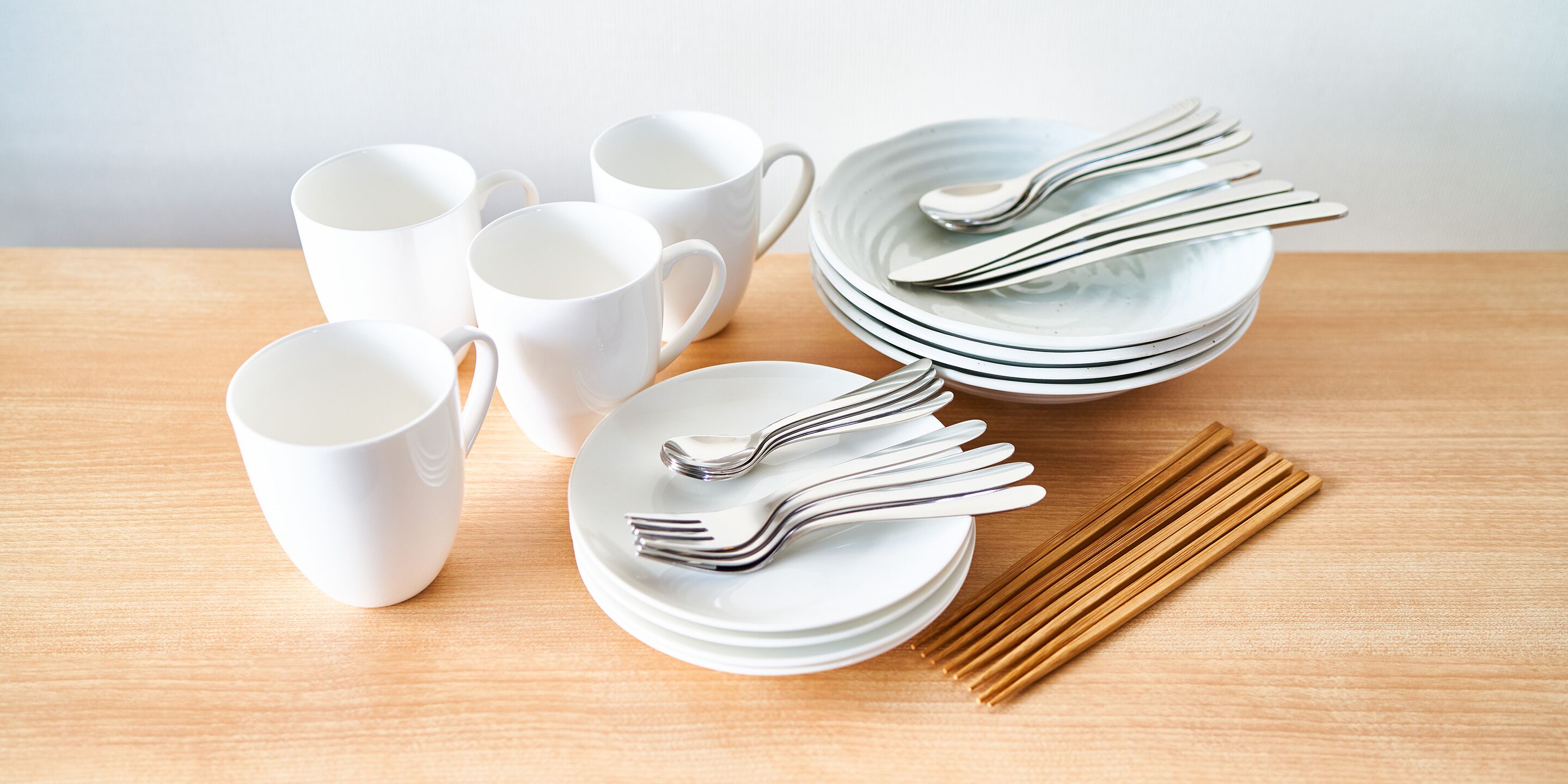 A set of white ceramic cups, plates, and silverware arranged on a wooden table.