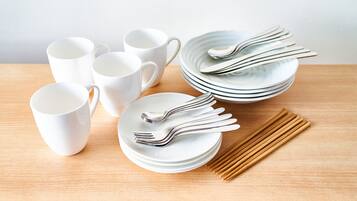 A set of white ceramic cups, plates, and silverware arranged on a wooden table.