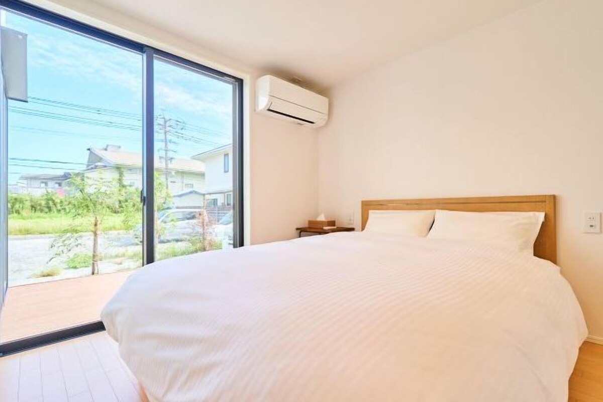 A bedroom with a large bed, a nightstand, an air conditioning unit, and a view of the outside.