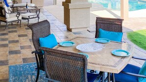 Ein Patio im Freien mit Pool, ausgestattet mit Korbstühlen und einem Tisch, mit Blick auf den Pool und Grünflächen.