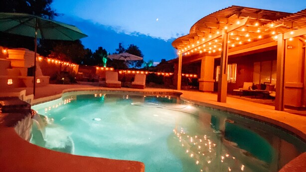 Ein Schwimmbecken mit Wasserspiel, umgeben von einer überdachten Terrasse mit Lichterketten.