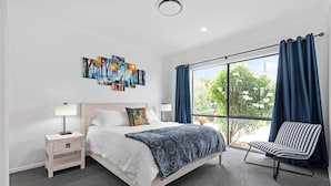 Un dormitorio moderno con una cama grande, mesitas de noche, una silla y un ventanal con cortinas.