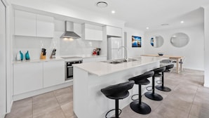 Una cocina moderna con armarios blancos, una isla central con taburetes y un horno empotrado, además de un lavamanos de acero inoxidable.