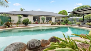 Una propiedad residencial con piscina, un patio cubierto y una casa de ladrillo con techo de tejas.