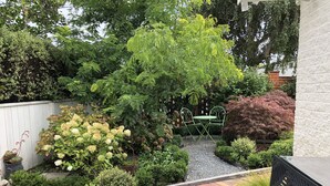 A well-maintained garden with a variety of plants, a small table with chairs, and a brick pathway. - Hidden Gem - Bed & Breakfast (Upper Hutt)