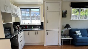 A compact kitchen with white cabinets, a black countertop, and a built-in dishwasher. - Hidden Gem - Bed & Breakfast (Upper Hutt)