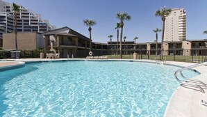Una piscina rodeada de palmeras y un edificio con varios balcones.