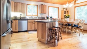 A kitchen with wooden cabinets, a stainless steel refrigerator, a central island with stools, and a dining table with chairs. - Summer Basecamp: Near Mt Baker, BBQ, AC, Fireplace (Glacier)