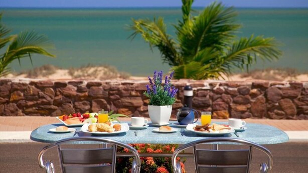 Una mesa dispuesta para el desayuno, una planta en maceta y vista al océano.