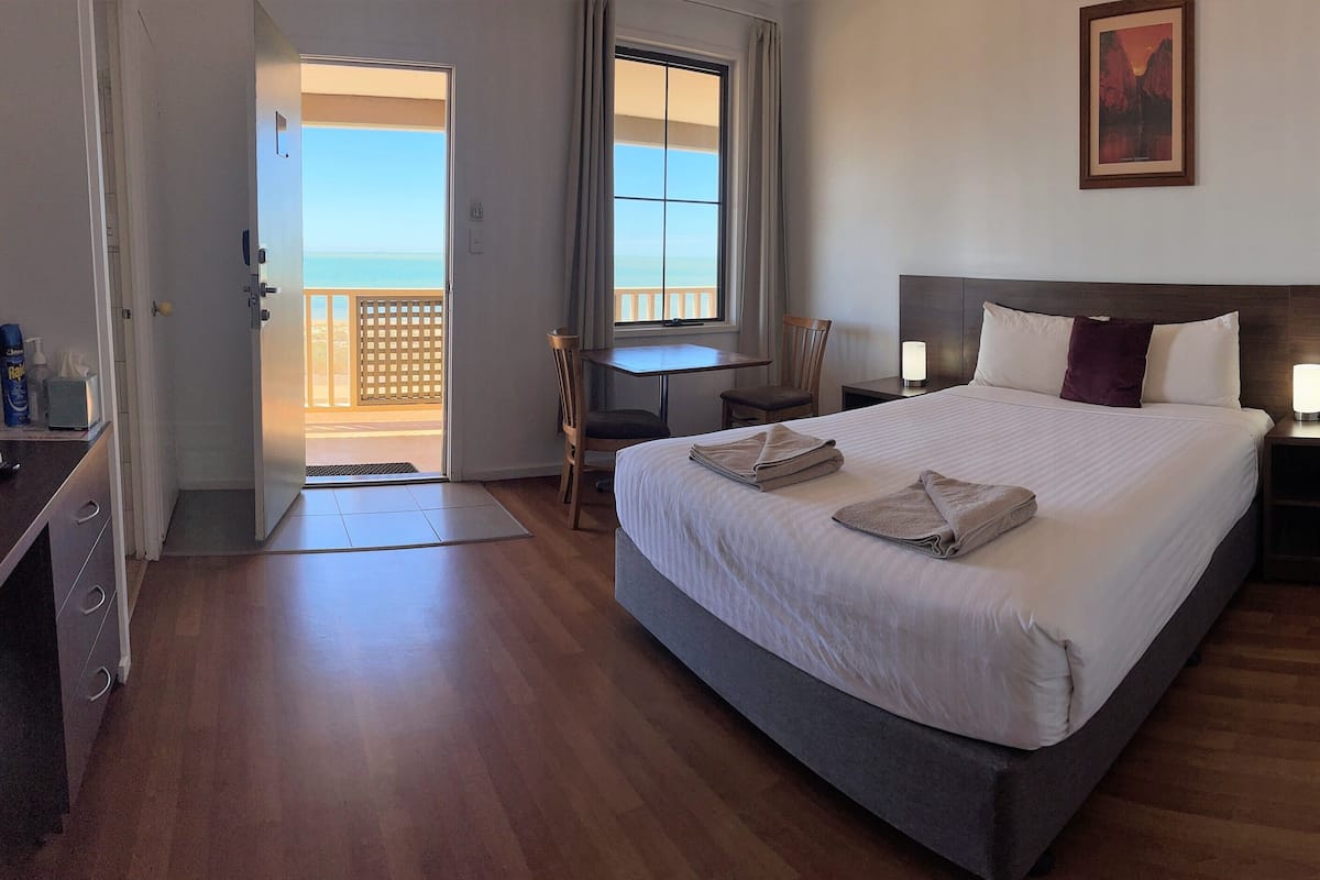 Hotelkamer met een bed, bureau, stoel, nachtkastje, televisie en balkon met uitzicht op zee.