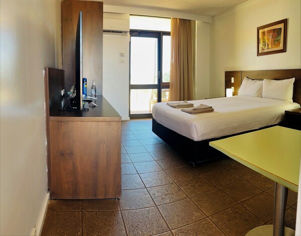 A hotel room with a bed, a desk, a mirror, a window with curtains, and a painting on the wall.