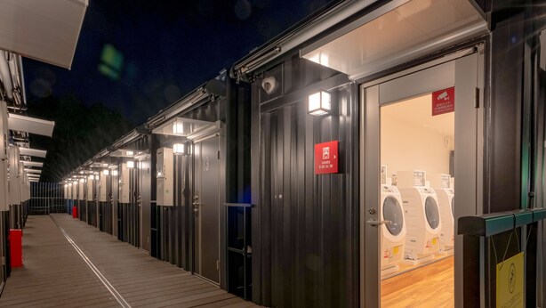 Een rij donkergekleurde hotelkamers, elk met een eigen deur en een wasmachine.