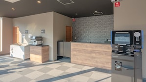 Een hotel receptie met een receptiebalie, een zelfbedieningskiosk en een koffieapparaat.