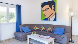 A modern living room with a grey sofa, colorful cushions, a white coffee table, and a painting on the wall.