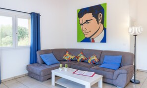 A modern living room with a grey sofa, colorful cushions, a white coffee table, and a painting on the wall.
