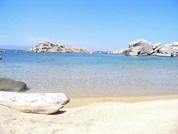 A beach with clear water, large rocks, and a boat.