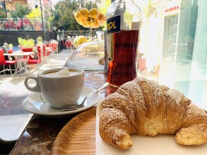 A table with a cup of coffee, a bottle of syrup, and a pastry. - Hotel Elysee (Tirana)
