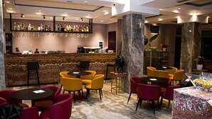 Un espace bar doté d’un comptoir en marbre, de plusieurs options d’assises, notamment des tables et des chaises rondes, ainsi que d’une variété de bouteilles et de verres exposés sur des étagères.