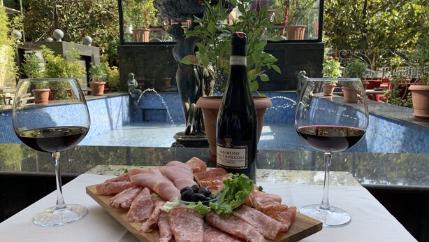 Une table avec une planche de charcuterie, deux verres de vin rouge et une bouteille de vin Amarone.