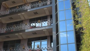 Un hôtel à plusieurs étages doté de balcons, de sièges en plein air et d’une façade en verre qui reflète le ciel.