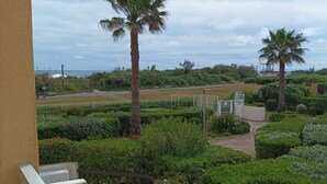 A balcony with a view of a landscaped garden, palm trees, and a distant building.