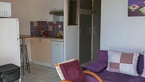A compact living space with a kitchenette, a dining area, and a seating area with a purple sofa and a wooden chair.