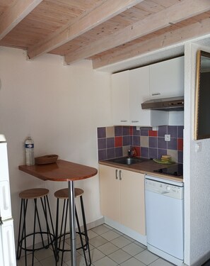 A compact kitchen with a wooden table, bar stools, a dishwasher, and a tiled backsplash. - Apt 40m² 1st line on beach Richelieu (Agde)