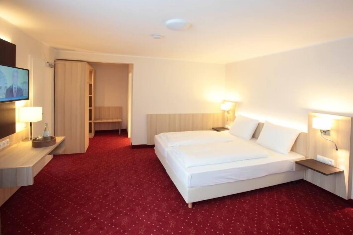 Habitació d'hotel amb un llit gran, dues taules de nit, una televisió i un terra amb moqueta vermella.