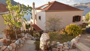 A coastal house with a red-tiled roof, white walls, and a stone pathway leading to the entrance.