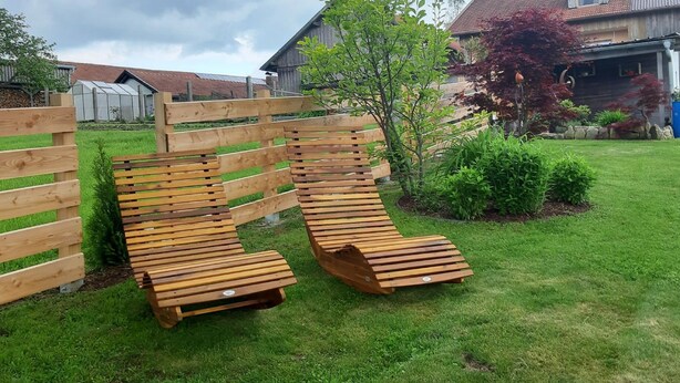 Eine hölzerne Bank in einem grünen Garten mit einem Holzzaun und einem kleinen Baum.