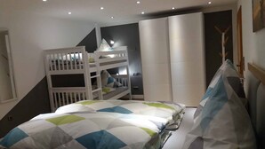 Ein Schlafzimmer mit Etagenbetten, einem Bett mit gestecktem Überwurf und einem modernen Design, das durch eine dunkle Akzentwand hervorgehoben wird.