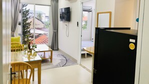 A modern room with a dining table, chairs, a TV, and a refrigerator. - New Hampton Hospitality - Cornelia Hotel & Apartment (Ho Chi Minh City)