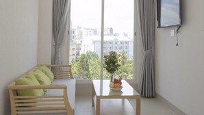 A modern living room with a wooden sofa, a glass dining table, and a TV mounted on the wall. - New Hampton Hospitality - Cornelia Hotel & Apartment (Ho Chi Minh City)