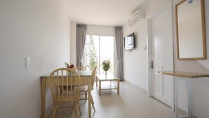 A hotel room with a dining area featuring a wooden table and chairs, a television mounted on the wall, and a door leading to another room. - New Hampton Hospitality - Cornelia Hotel & Apartment (Ho Chi Minh City)