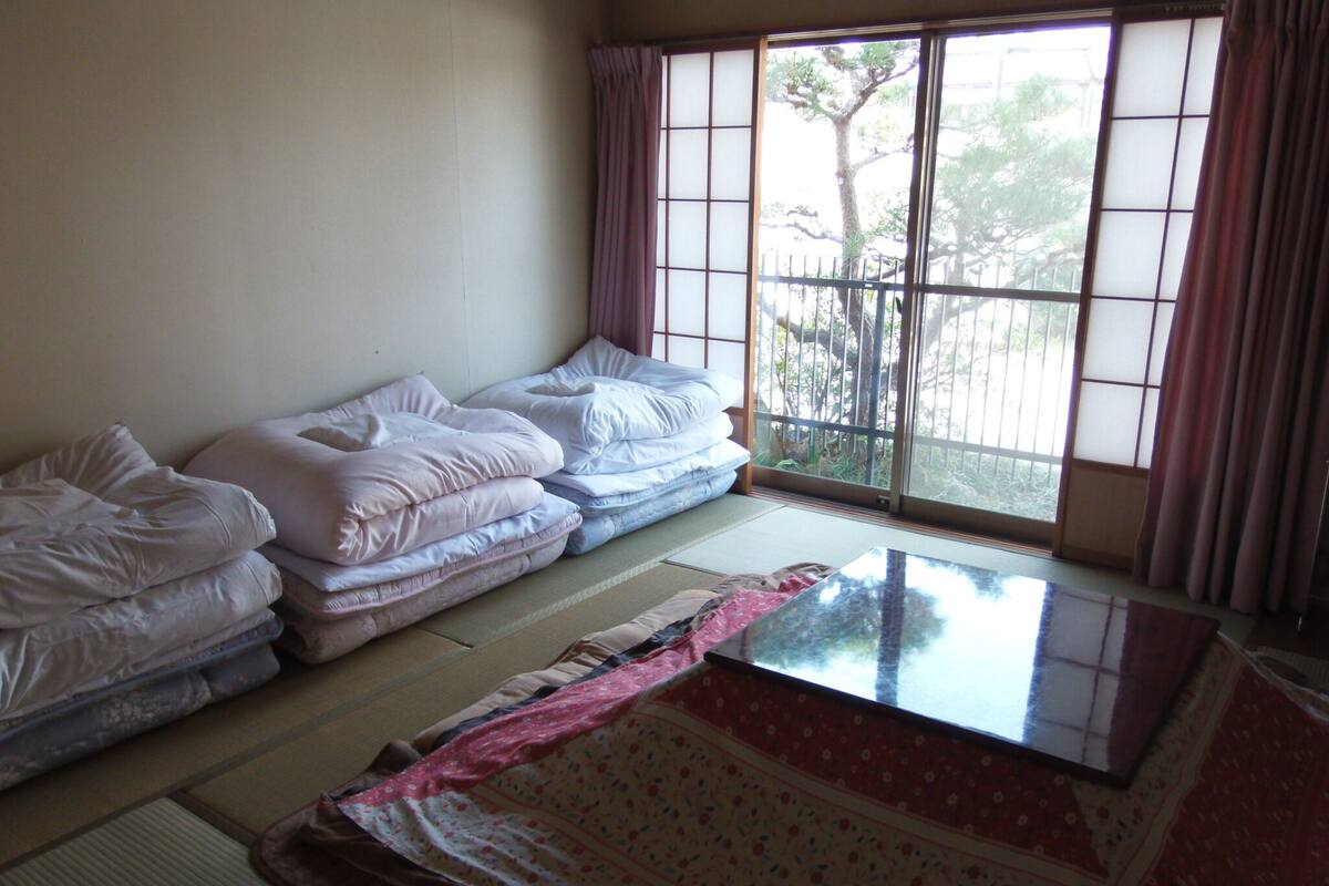 A room with tatami mats, a futon bed, and a sliding door to a garden.