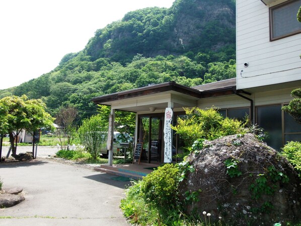 A building with a covered entrance, surrounded by greenery and a mountain in the background. - Nunobikikannon Onsen (Tomi)