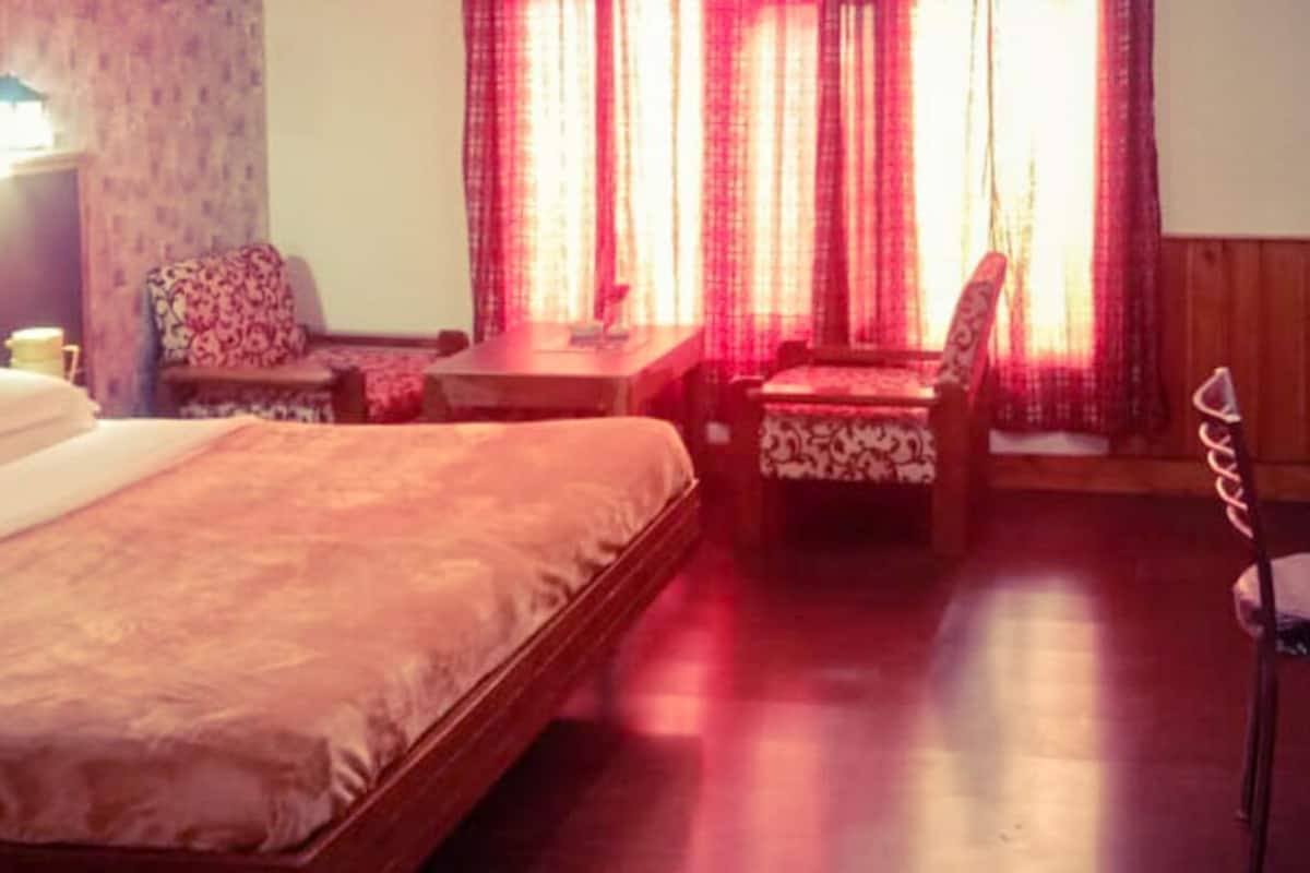 Quarto de hotel com uma cama, duas cadeiras, uma mesinha e uma escrivaninha.