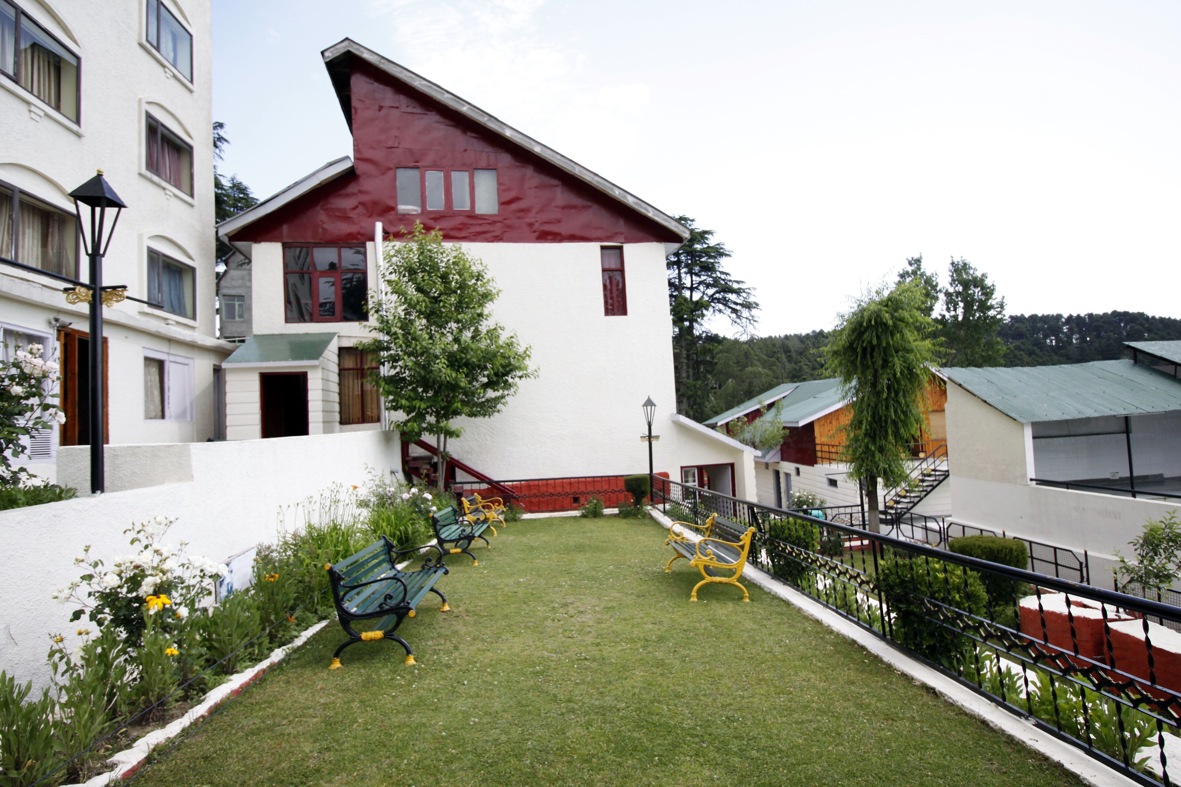 A courtyard with a red-roofed building, green benches, and a small tree.