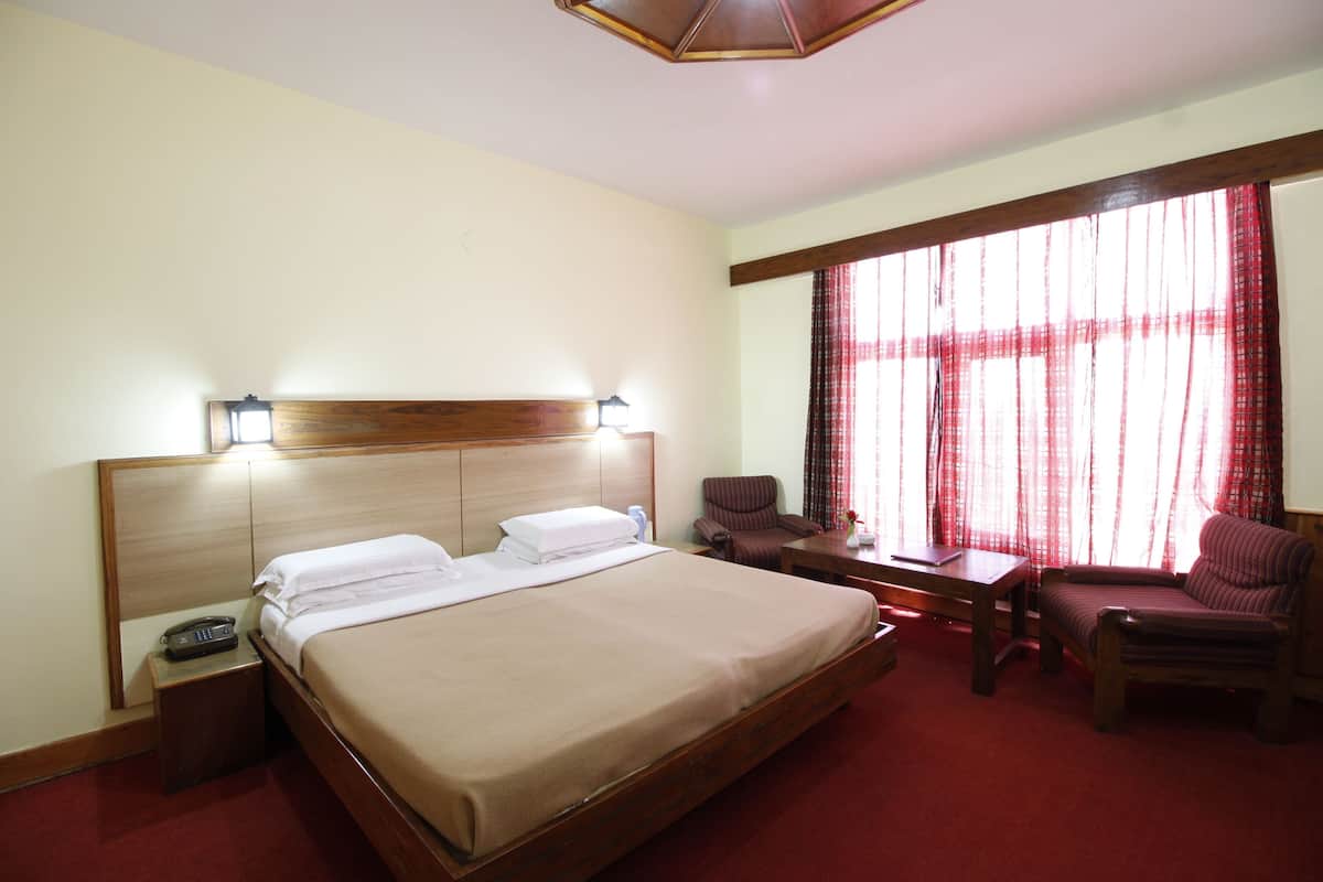 Quarto de hotel com uma cama grande, mesas de cabeceira, escrivaninha, cadeira e janela com cortinas.