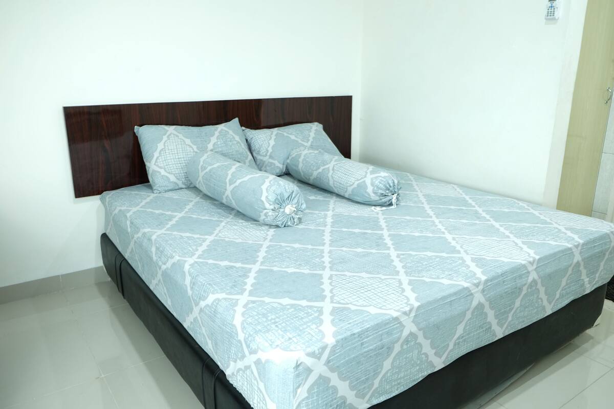 A bed with a patterned bedspread and two pillows, a wooden headboard, and a tiled floor.