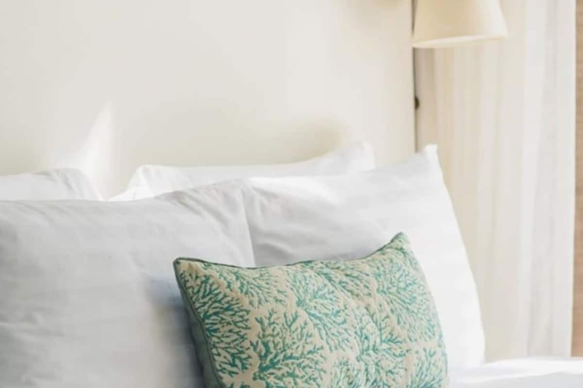 A bed with white bedding and a single decorative pillow with a leaf pattern.