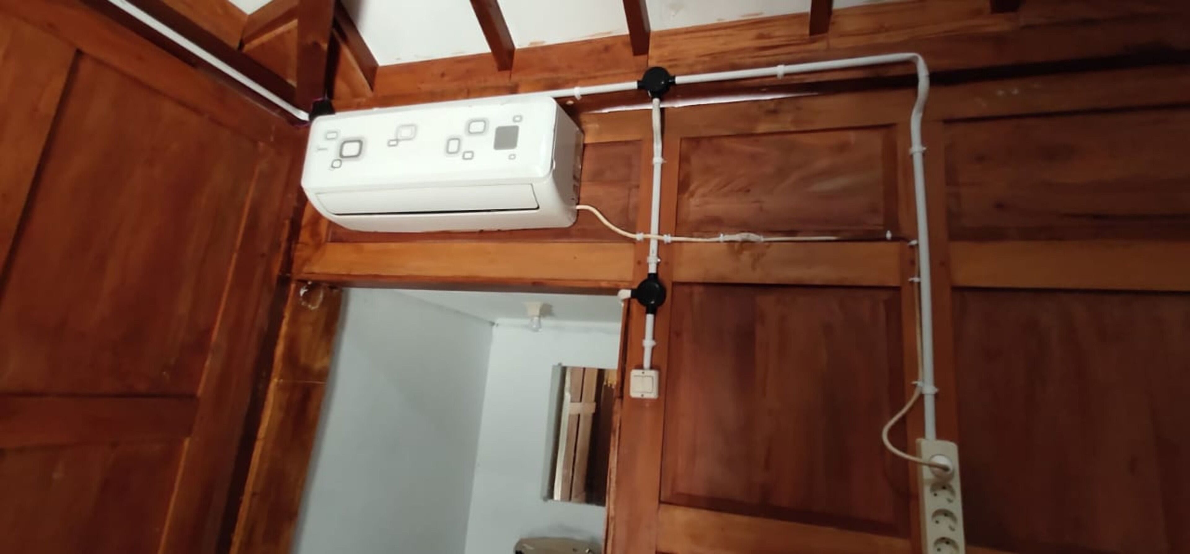 Eine weiße Elektroleitung an einer Holzwand, mit sichtbarer Verkabelung und einer Steckdose darunter.